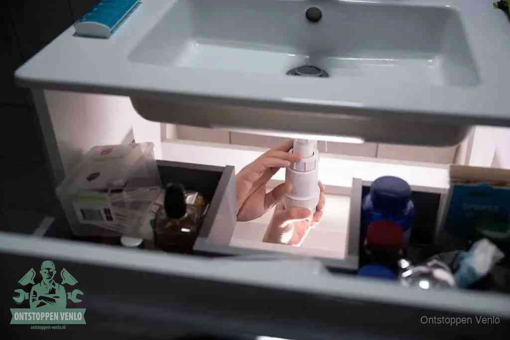 Een pompfles met zeep boven een wastafel, de heet water en afwasmiddel-methode om een vetprop in de afvoer los te maken in Venlo