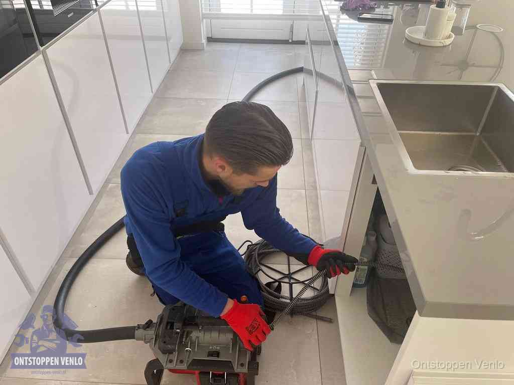 Een monteur ontstopt de keukenafvoer onder de spoelbak met een elektrische veermachine in Venlo