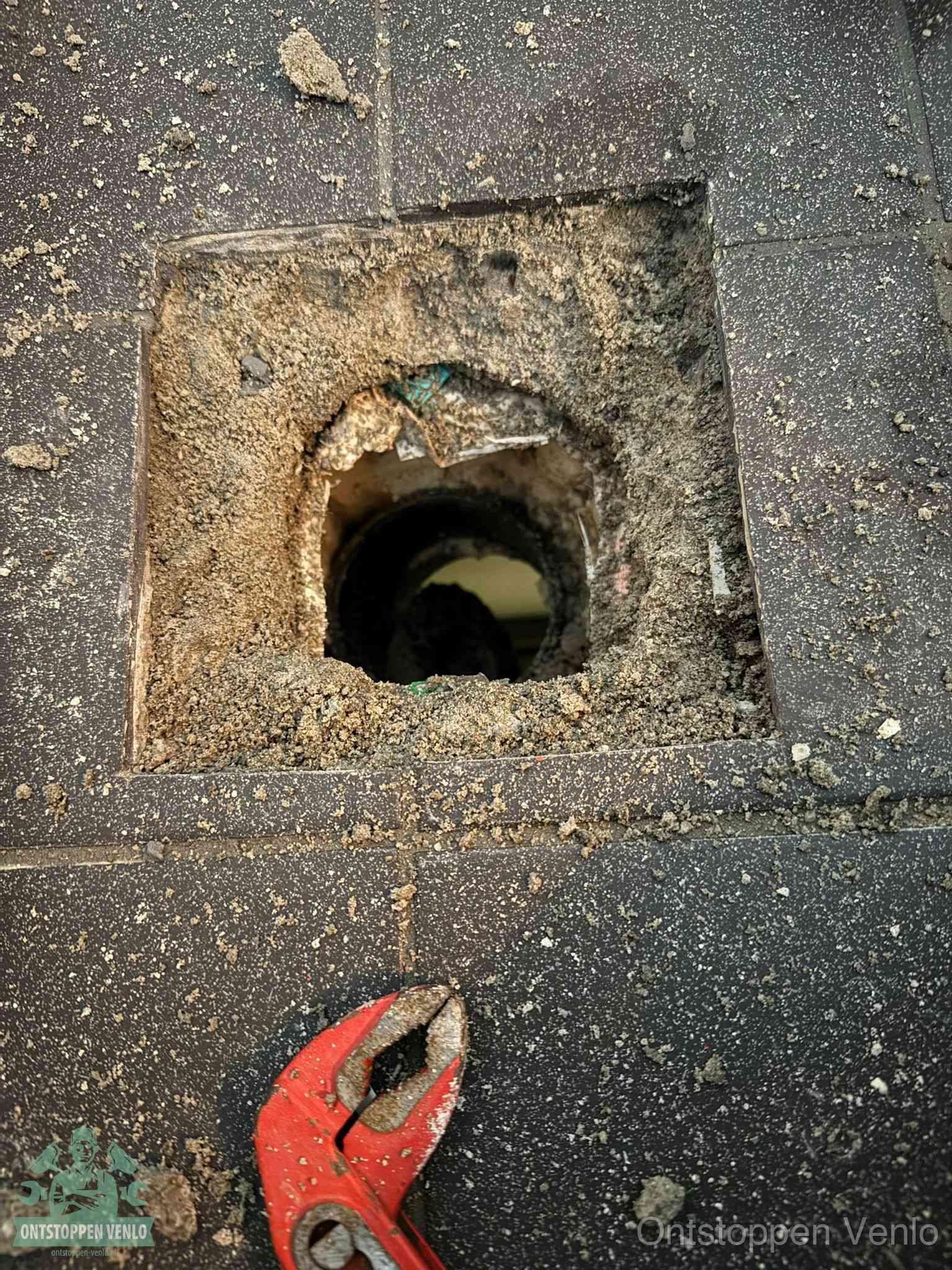 Een geopend rioolputje in een betontegelvloer met losgemaakt rooster en een zichtbare ronde afvoerbuis, het achterhalen waar de afvoerverstopping zit in Venlo