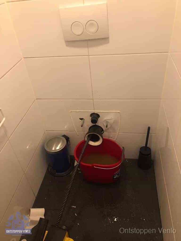 Een ontstopte wand-wc met verwijderde toiletpot waar een ontstoppingsveer in de wanduitgang verdwijnt, het achterhalen waar de verstopping zit in Venlo