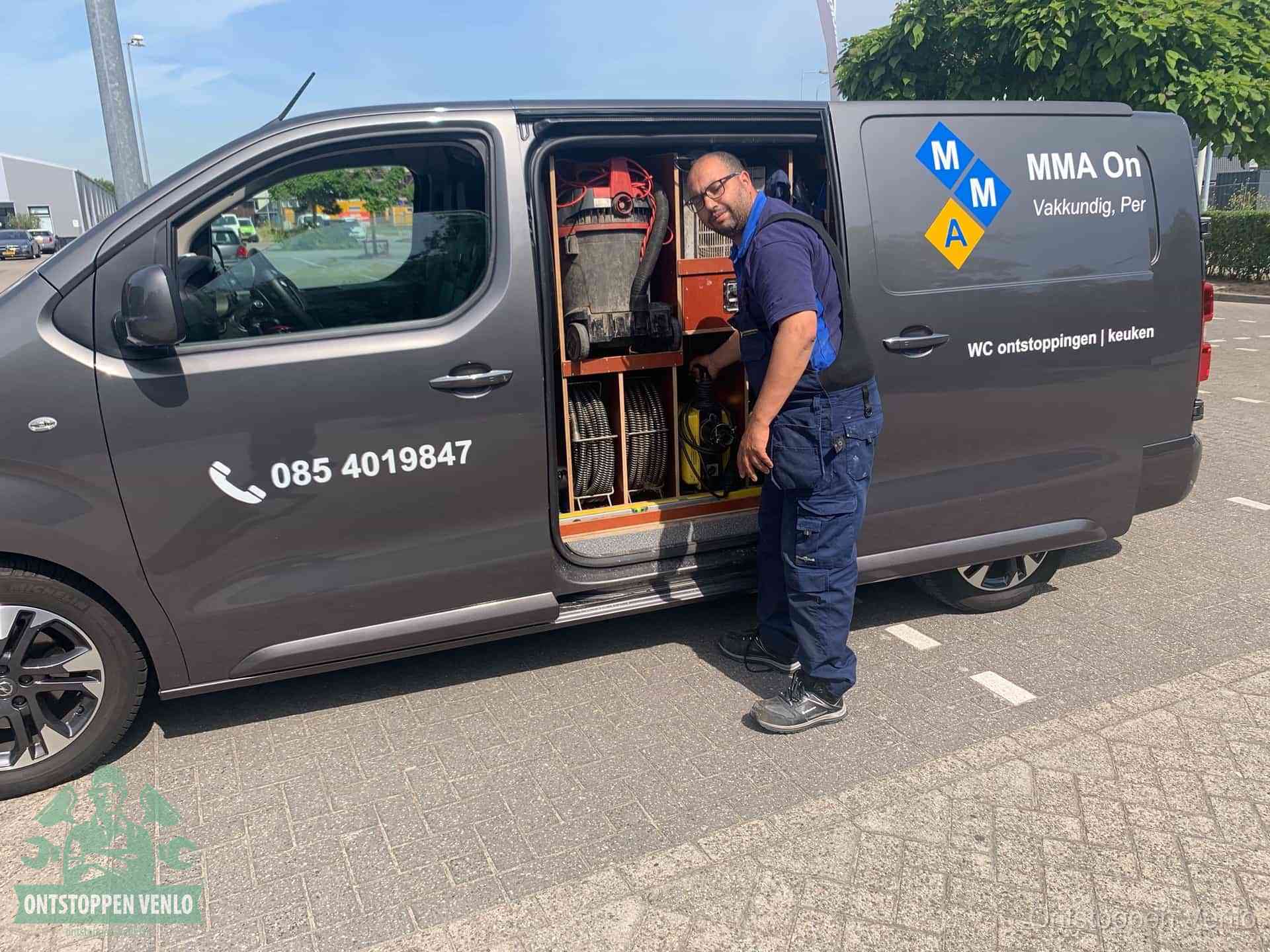 Een monteur bij de open schuifdeur van zijn bedrijfsbus op een parkeerplaats, klaar om de oorzaak van terugkerende afvoerverstoppingen aan te pakken in Venlo
