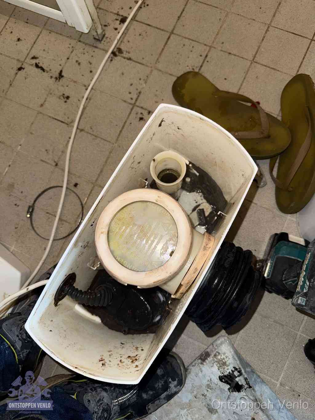 Een gedemonteerde toiletpot op de vloer met ontstoppingsveer en gereedschap ernaast, het verwijderen van een vastzittend voorwerp uit de wc in Venlo