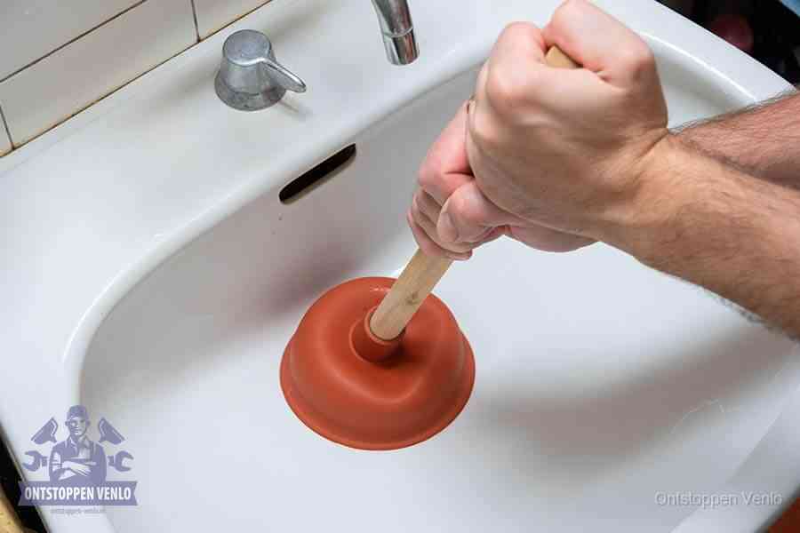 Twee handen gebruiken een rode rubberen plopper op een sanitair-afvoer om het toilet te ontstoppen in Venlo